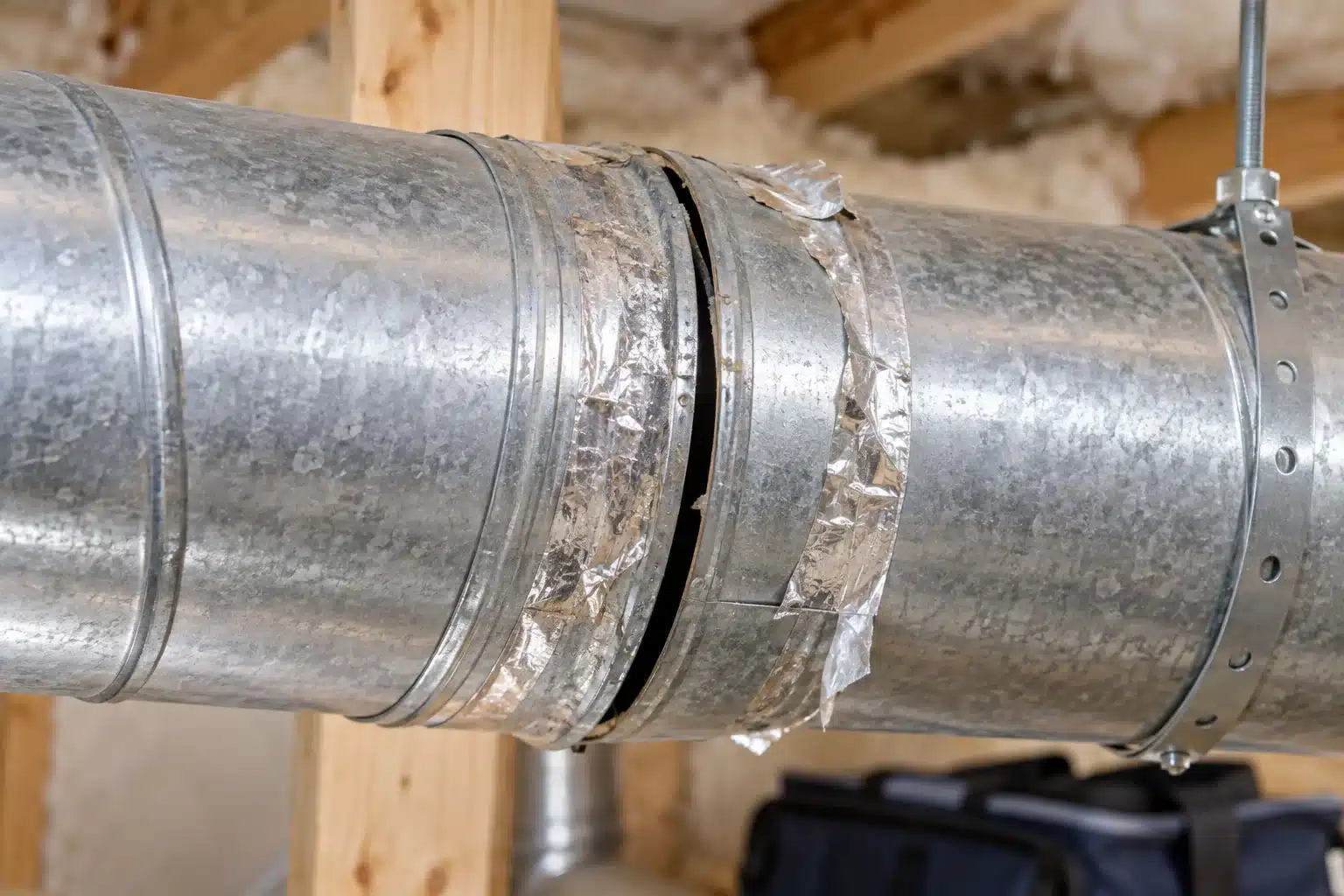 Gap at a round metal HVAC duct joint with peeling foil sealing tape.